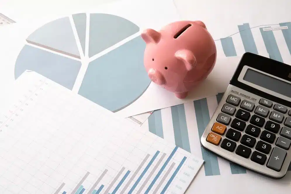 A imagem mostra uma composição com um gráfico de pizza, um gráfico de barras, uma calculadora e um cofre em formato de porco. Esses elementos visuais sugerem que o conteúdo está relacionado a aspectos financeiros, contábeis ou tributários. Essa imagem é relevante para o artigo "OBRIGATORIEDADE DO CEST (CÓDIGO ESPECIFICADOR DA SUBSTITUIÇÃO TRIBUTÁRIA)", pois ela ilustra visualmente alguns dos principais conceitos e ferramentas utilizados na gestão e contabilidade tributária.