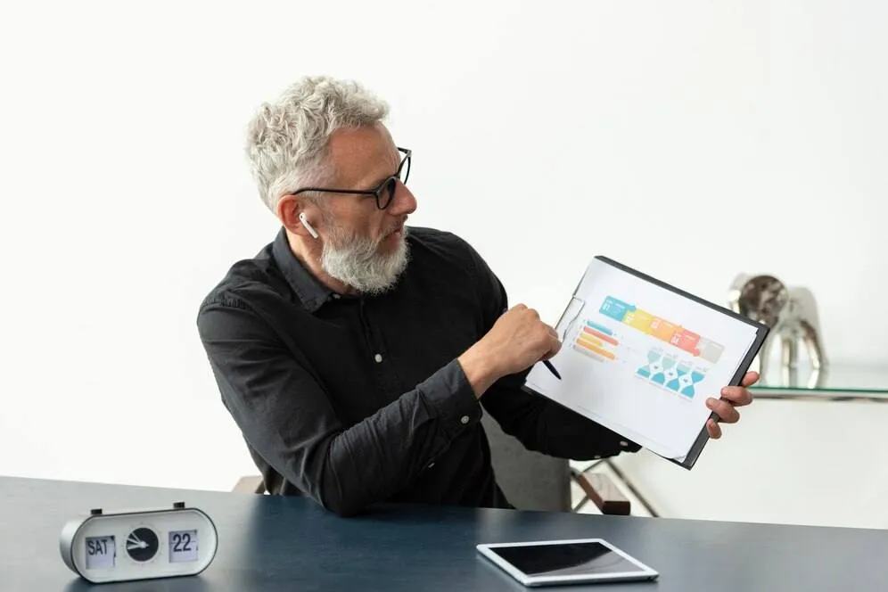 A imagem mostra um homem de negócios analisando um relatório com gráficos, simbolizando a importância da monitoração e do gerenciamento de KPIs (Indicadores de Desempenho Chave) na logística. No contexto do artigo, isso reflete a necessidade de acompanhar e otimizar indicadores-chave, como o tempo de entrega, a precisão da entrega, o custo da logística e a satisfação do cliente, para melhorar o desempenho e a eficiência das operações logísticas da empresa.