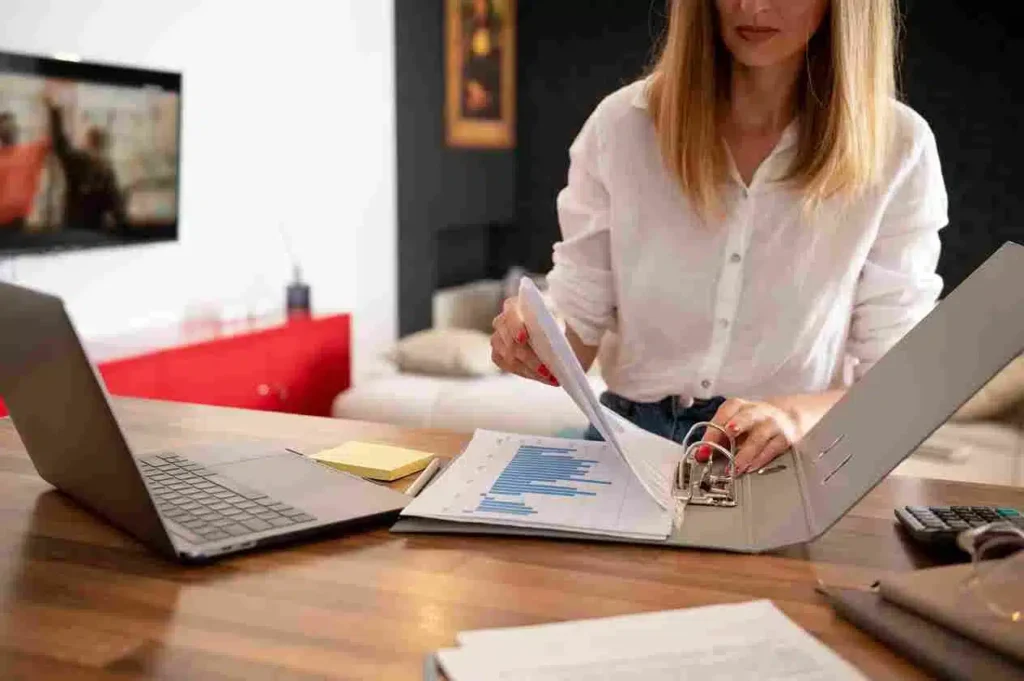 A imagem mostra uma mulher trabalhando em seu computador, analisando documentos e gráficos em uma mesa de escritório, sugerindo que o artigo abordará tópicos relacionados a soluções fiscais de PDV, como gestão e controle financeiro de transações, conformidade fiscal e tributária, análise de dados e relatórios, e integração com sistemas contábeis e de gestão, fornecendo orientações e melhores práticas para que empresas e comerciantes possam implementar e gerenciar efetivamente seus sistemas de PDV, atendendo aos requisitos legais e fiscais.