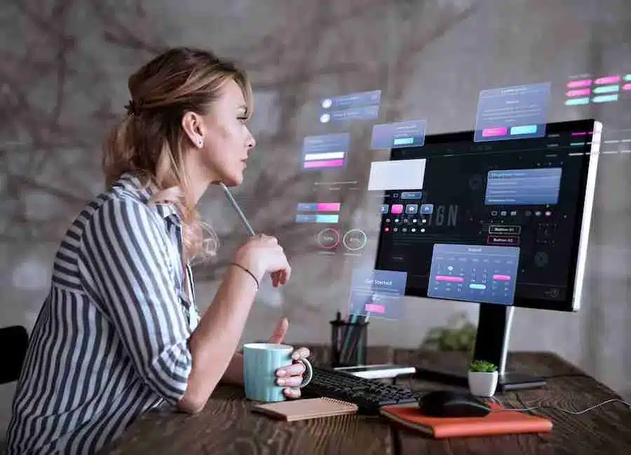 A imagem mostra uma mulher trabalhando em um computador com uma interface gráfica complexa e cheia de informações. Ela parece estar analisando dados ou interagindo com um sistema de gerenciamento empresarial (ERP). Essa imagem é relevante para o artigo "ONCLICK apresenta novas funcionalidades do ERP líder de e-commerce", pois ela sugere a utilização de uma plataforma tecnológica avançada para a gestão de negócios online.
