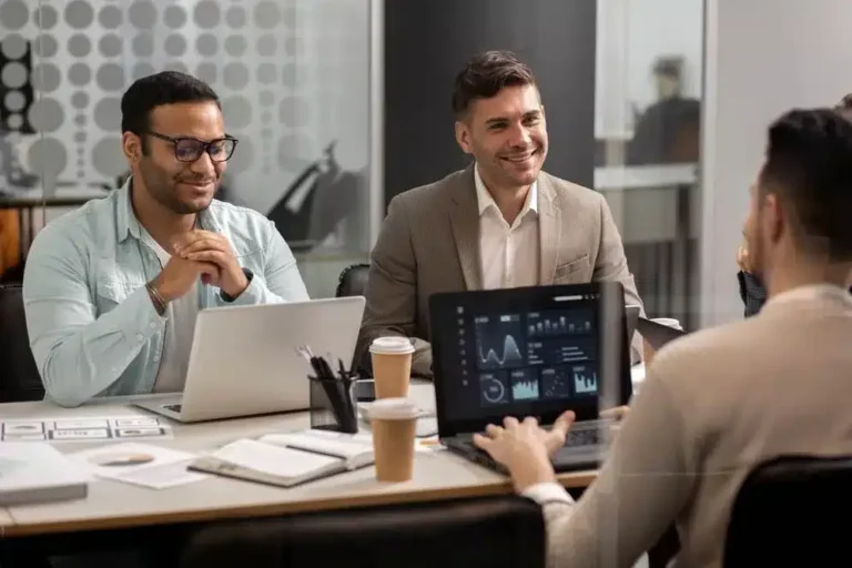 A imagem mostra um grupo de profissionais reunidos em uma reunião de trabalho, discutindo e analisando dados apresentados em um tablet. Ilustra a importância de antecipar as tendências em gestão, pois a equipe parece estar envolvida em um processo de análise e discussão de informações que podem subsidiar decisões estratégicas e melhorar a eficácia da gestão.