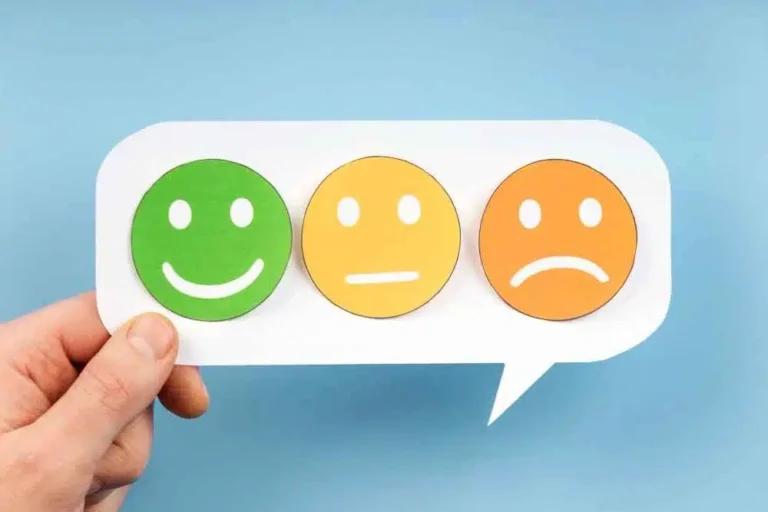 Mão segurando um cartão de fala com emojis de rosto coloridos, representando feedback de clientes. Simboliza a importância de lidar com avaliações negativas e a necessidade de gerenciamento de feedback em e-commerce.
