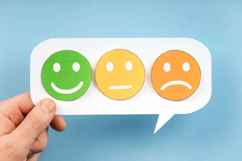 Mão segurando um cartão de fala com emojis de rosto coloridos, representando feedback de clientes. Simboliza a importância de lidar com avaliações negativas e a necessidade de gerenciamento de feedback em e-commerce.