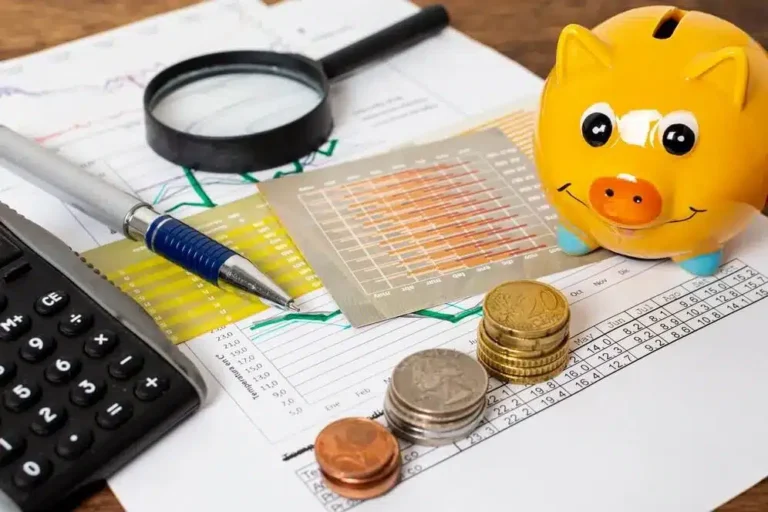 Imagem exibe um ambiente de trabalho financeiro, com um cofre de porco, moedas, uma lupa, um pen, um calculator e papéis com gráficos e tabelas, representando a gestão de finanças e contabilidade. No contexto do artigo sobre mudanças na EFD-Reinf (Declaração de Informações de Contribuintes com Regime de Tributação Substitutiva), isso reflete a importância de estar atualizado com as novas regras e requisitos fiscais, para que os negócios possam cumprir adequadamente suas obrigações e aproveitar ao máximo as facilidades oferidas por essa modalidade tributária.