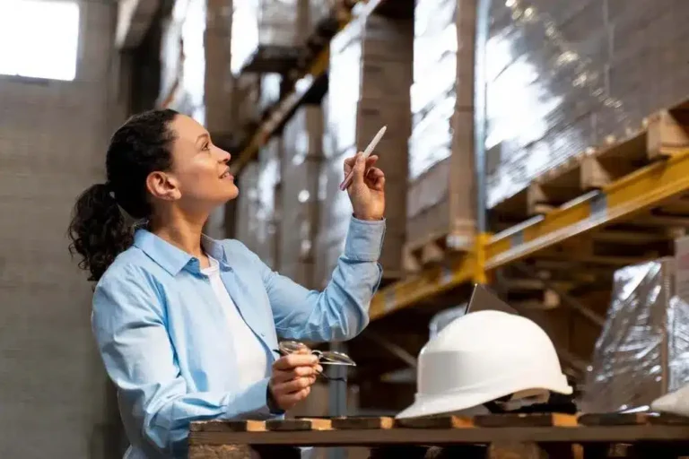 A imagem mostra uma gerente de logística em uma fábrica, anotando informações, simbolizando a preparação e o planejamento para o período de final de ano. No contexto do artigo, isso reflete a importância de se preparar antecipadamente para o aumento da demanda e do volume de entregas durante essa época, garantindo que as operações de logística sejam eficientes, os estoques sejam adequados e os prazos de entrega sejam cumpridos, para evitar atrasos e manter a satisfação dos clientes.