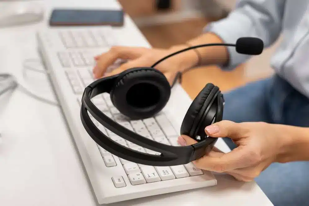 A imagem mostra uma pessoa usando um fone de ouvido com microfone, provavelmente realizando atendimento ao cliente ou suporte técnico. A imagem ilustra a importância do atendimento e suporte ao cliente no contexto do pós-venda, especialmente em períodos de alta demanda, como a Black Friday, para encantar e fidelizar os novos clientes adquiridos.