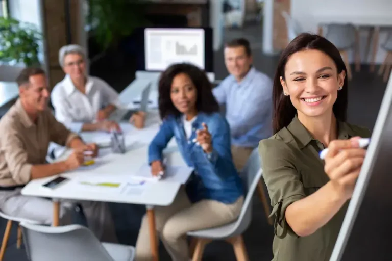 A imagem mostra uma reunião de negócios em um ambiente de trabalho moderno e agradável. Cinco indivíduos estão sentados em torno de uma mesa, com documentos e dispositivos digitais à mão, discutindo e compartilhando ideias. A mulher na frente da imagem está sorrindo e apontando para um notebook, o que indica que ela está apresentando ou discutindo algo com os colegas. No contexto do artigo "Oportunidades para empreender em 2023: o que o novo ano nos reserva", a imagem pode ser usada para ilustrar a colaboração e a inovação como chaves para o sucesso empresarial no ano novo.