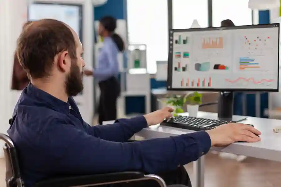 Homem em cadeira de rodas trabalhando em um escritório moderno, analisando gráficos complexos de desempenho e indicadores de qualidade em um monitor de computador. A imagem representa a inclusão e a precisão técnica de um Sistema de Gestão da Qualidade (SGQ), com foco em monitoramento de dados, melhoria de processos e automação de indicadores para empresas que buscam certificações como a ISO 9001.