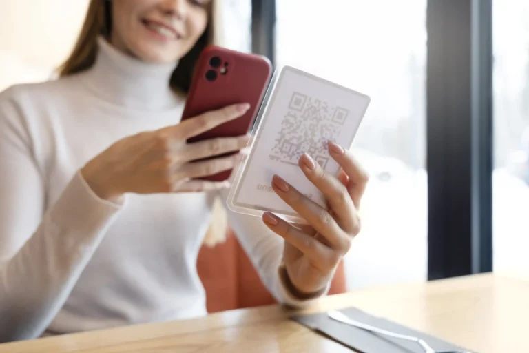Mulher sorridente em ambiente corporativo utiliza smartphone para escanear um QR Code de pagamento. A imagem ilustra a facilidade do Pix Automático no B2B para transações recorrentes, automação financeira e liquidação imediata em estabelecimentos físicos e digitais. Foco nas mãos segurando o celular e o código, representando tecnologia financeira e agilidade empresarial.