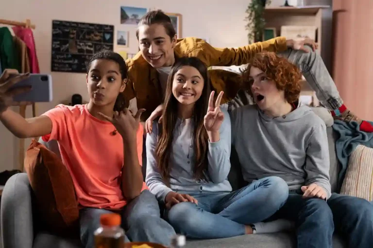 Grupo de jovens da geração Z tirando selfie no sofá com smartphone, representando comportamento digital, consumo online, redes sociais e hábitos de compra da geração Z em comparação com outras gerações.